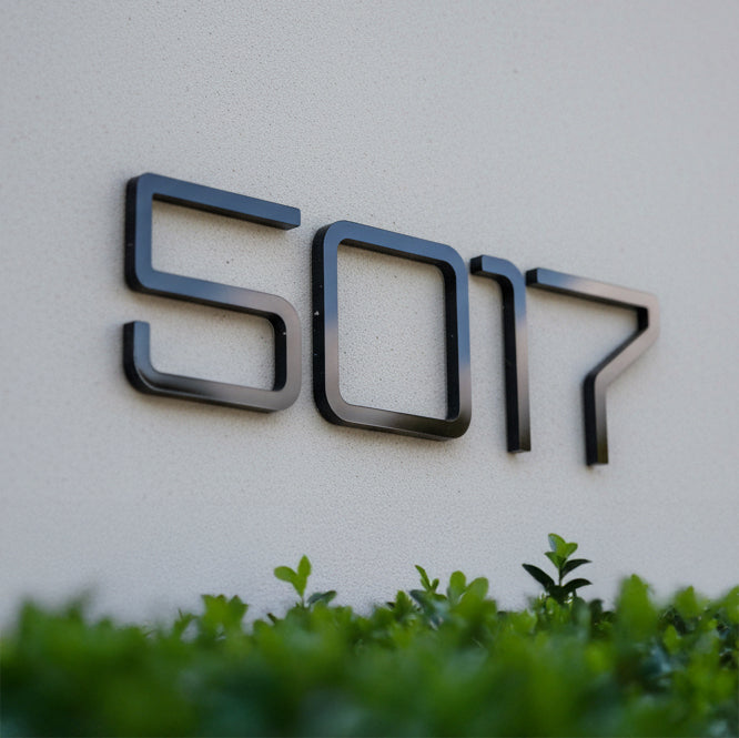 Modern house number '5017' on a light-colored wall with greenery at the bottom.