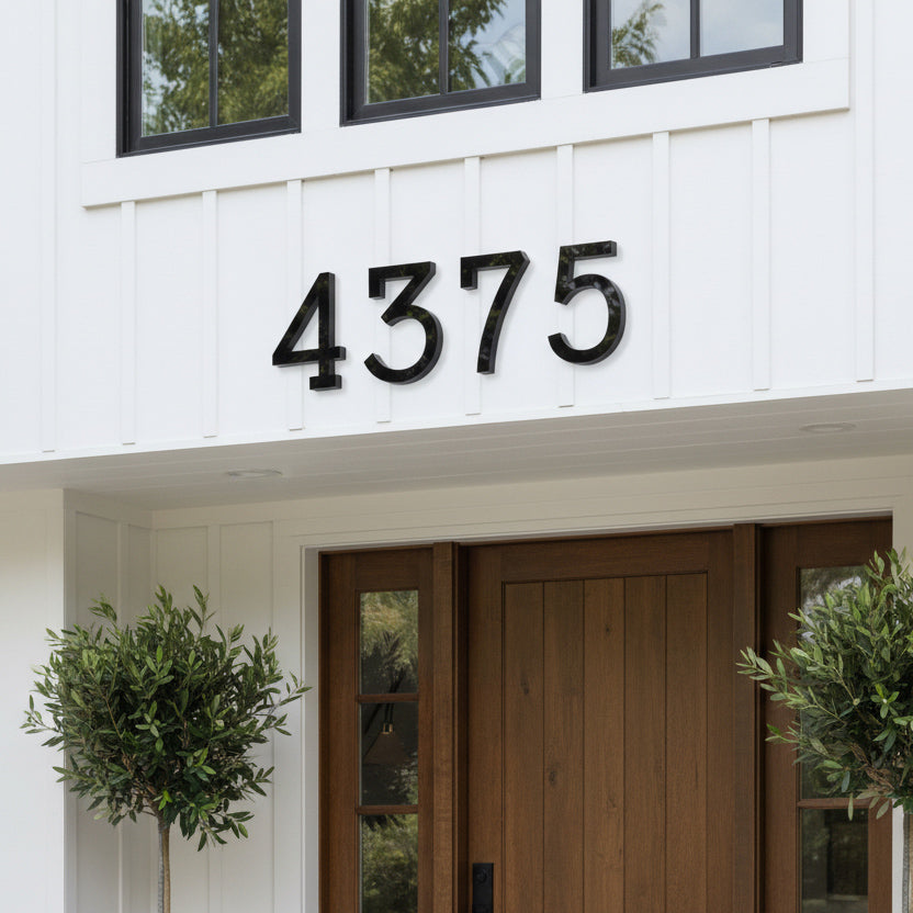 black House number '4375' on a white house with a wooden door and greenery.