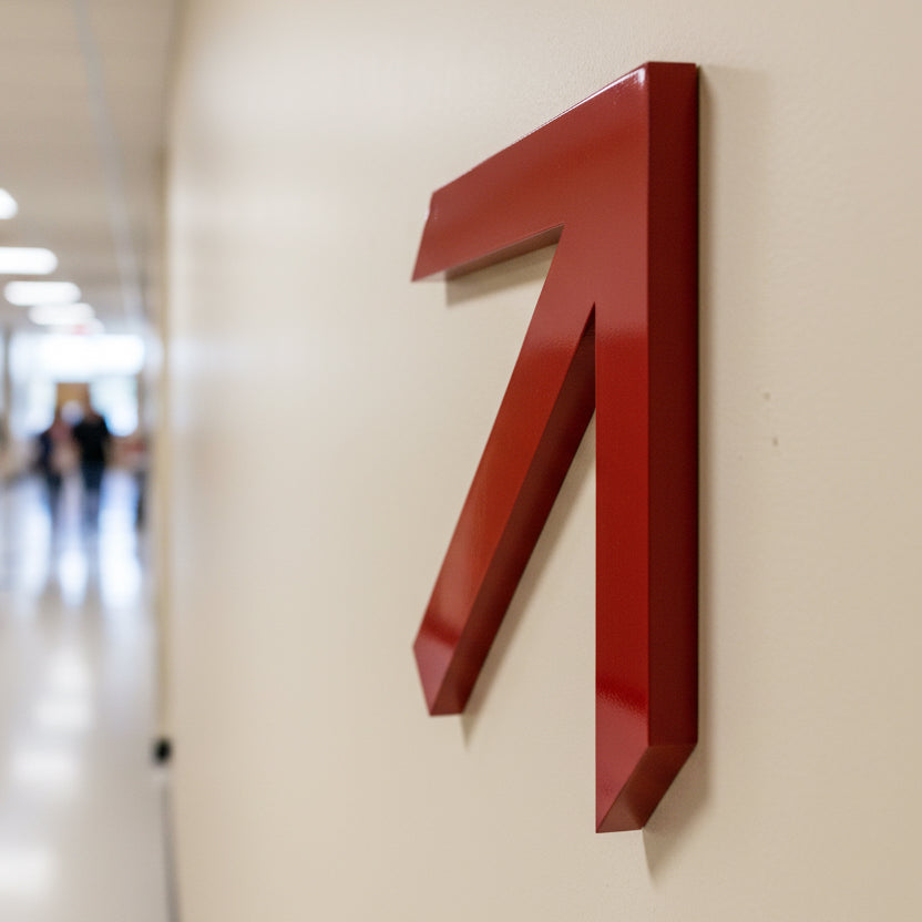 Red arrow-shaped sign on a beige wall with a blurred hallway in the background