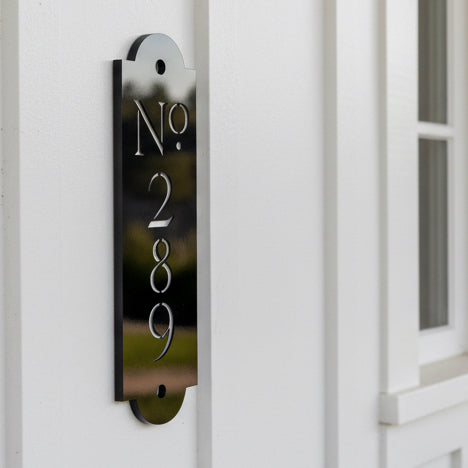 A black traditional style house number sign mounted on a white farmhouse