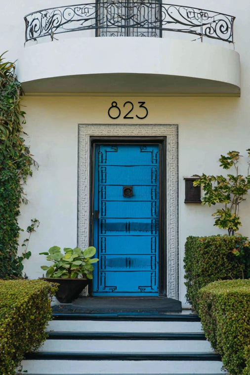 Blue door with decorative number '823' in black metal on a white building facade.