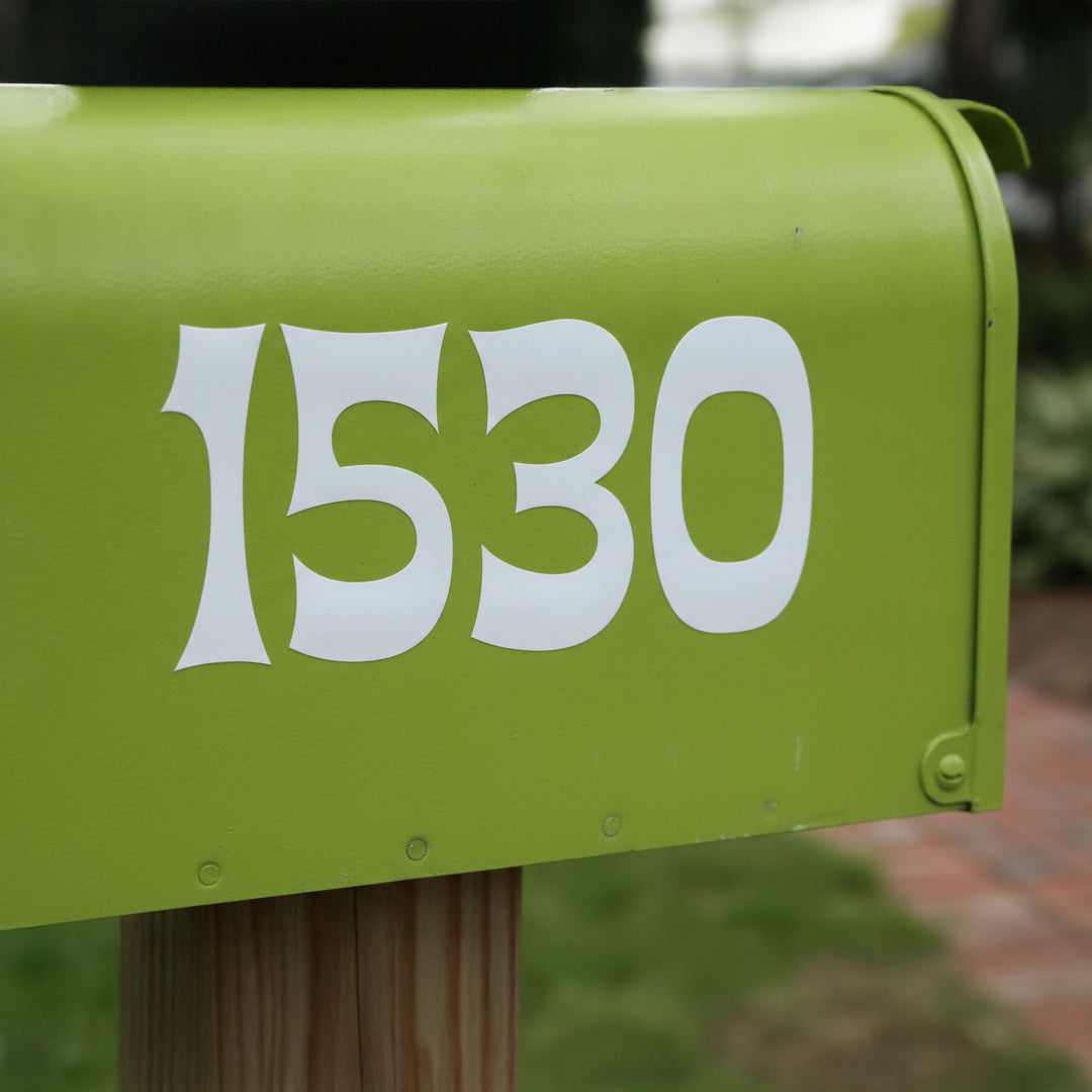 A close-up of a bright lime green mailbox mounted on a wooden post, featuring large white stylized numbers '1530' on the front, with a blurred outdoor background.