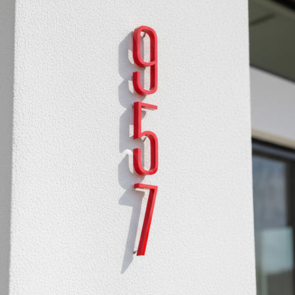 Red house numbers '957' on a white wall
