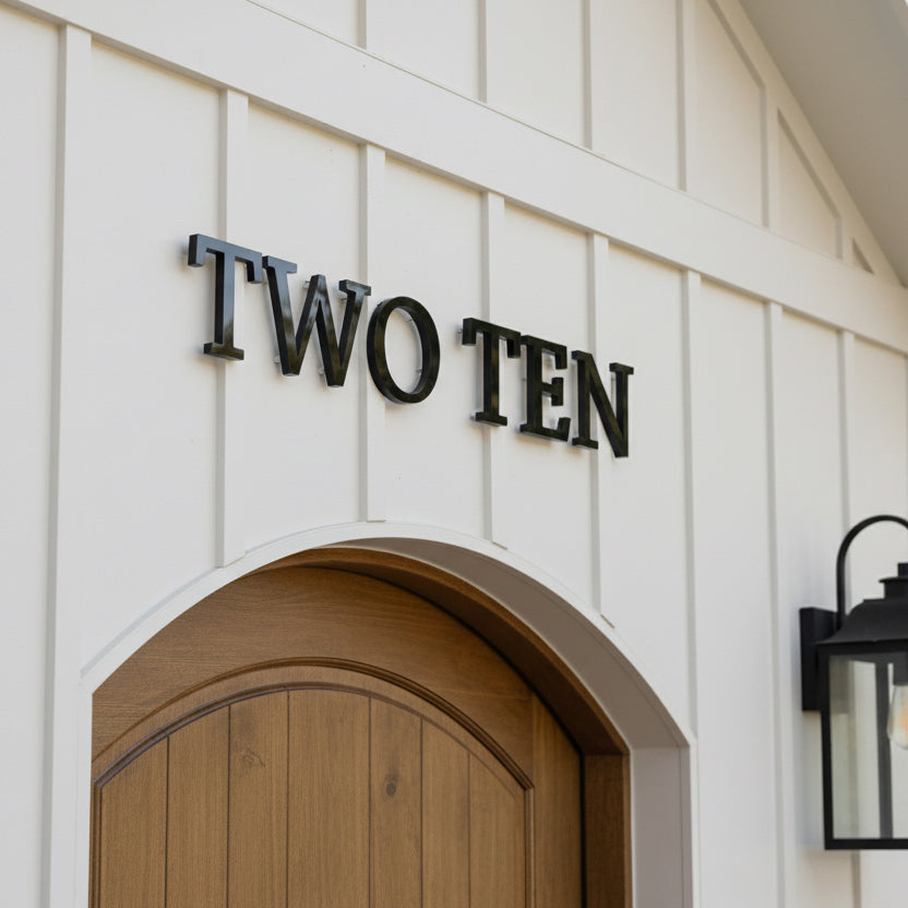 House number 'TWO TEN' on a white wall with a wooden door.