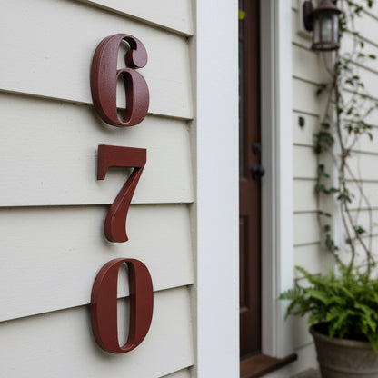 House numbers '670' on a house exterior with a plant and door frame.
