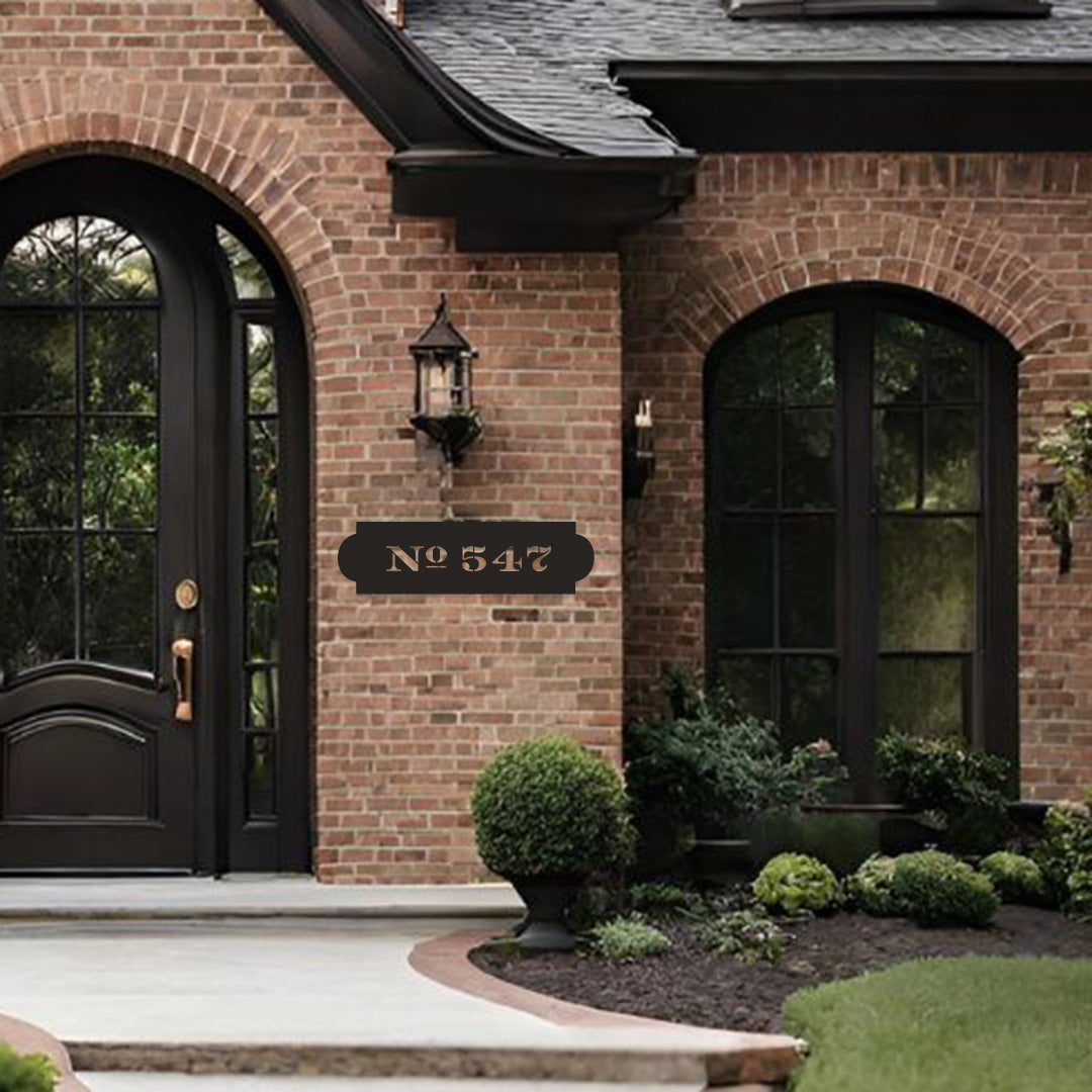 Traditional bronze address sign with "No 547" cut out of the metal on a red brick house with black trim and door