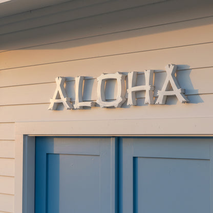 Metal 'ALOHA' sign on a building with a blue door.