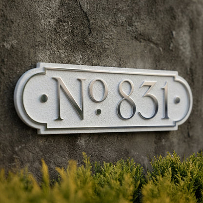 Decorative house number plaque displaying No.831 with raised lettering on textured concrete wall. Shown in: White · Cast Aluminum