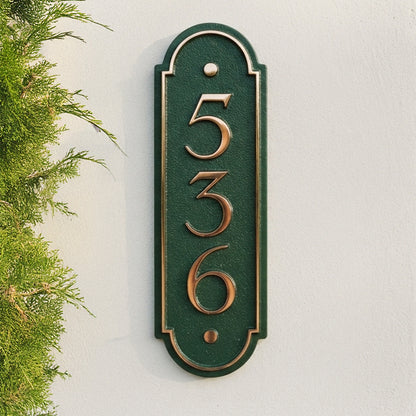 Vertical bronze house number plaque displaying 536 on green background with raised border detail on white wall. Shown in: Bronze · Cast Aluminum