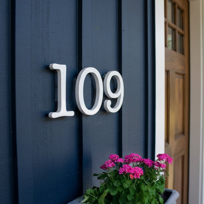 House number '109' on a blue door with pink flowers in the foreground