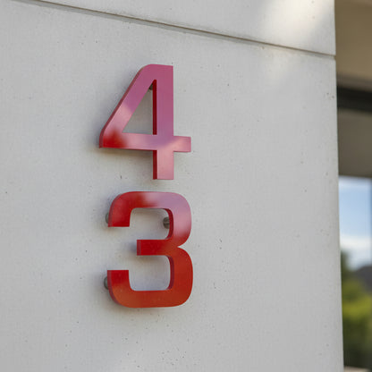 Red 3D house number '43' mounted on a light gray concrete exterior wall.