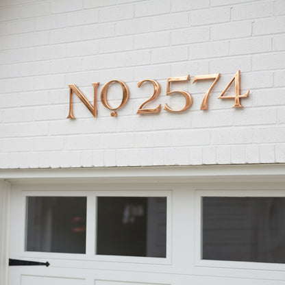 Copper house number '2574' on a white brick wall above a door.