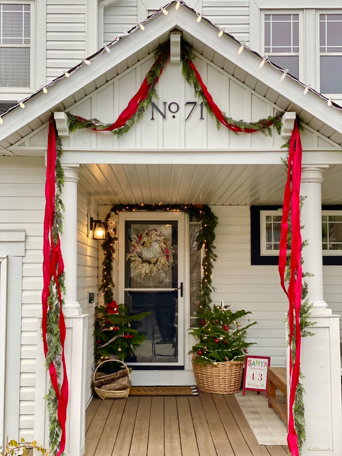 Decorative front porch of a house with Christmas decorations, including red ribbons and potted trees.