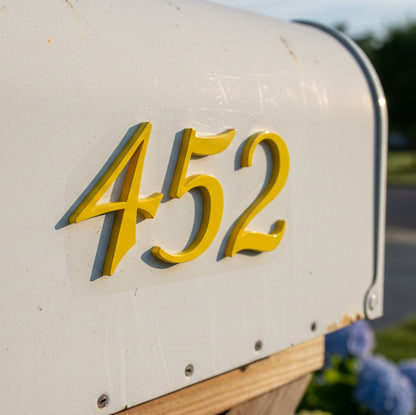 White mailbox with yellow numbers '452' on a blurred outdoor background